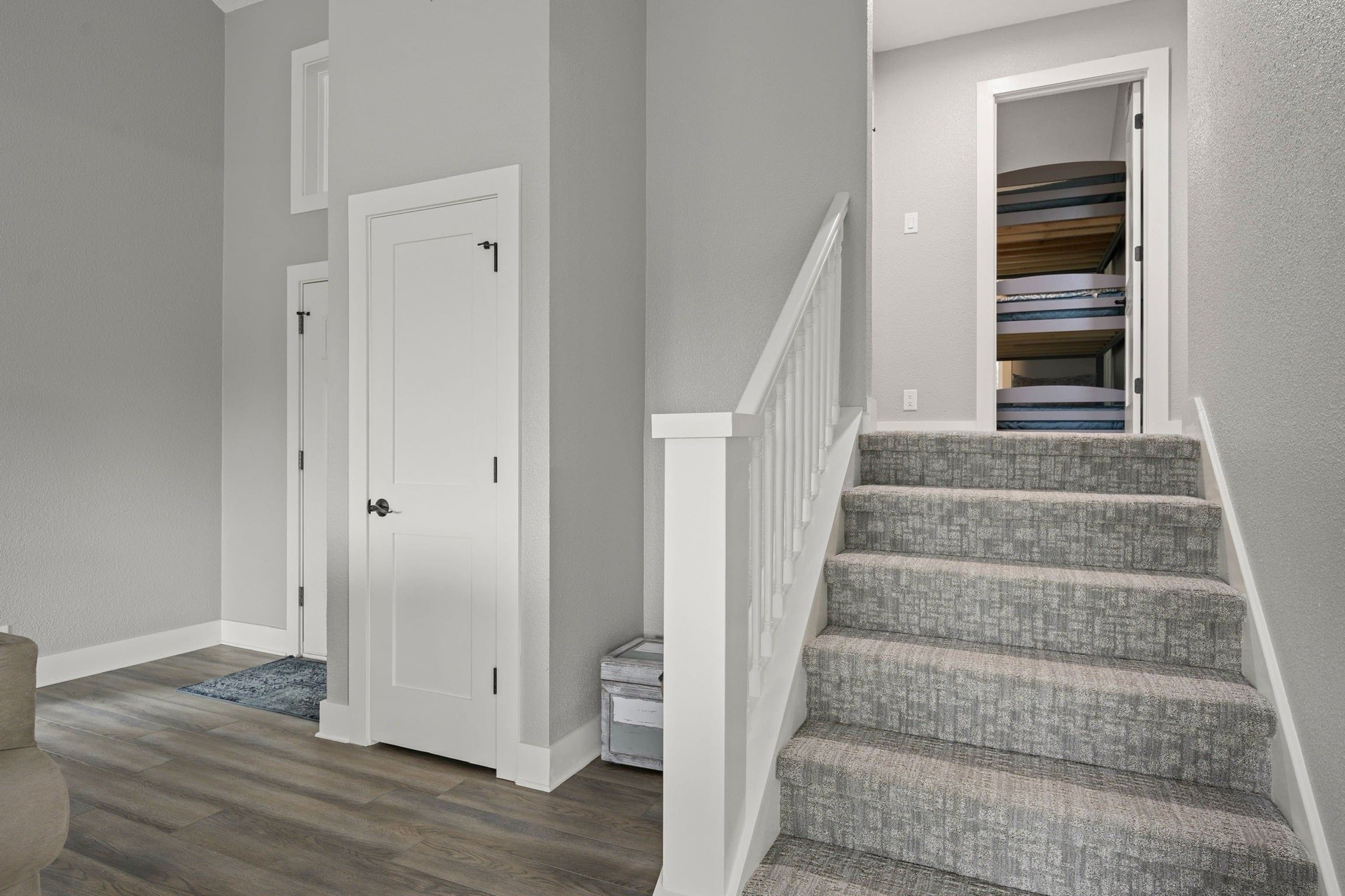 A hallway with a white door, a staircase with gray carpeted steps, and a small rug on the floor.