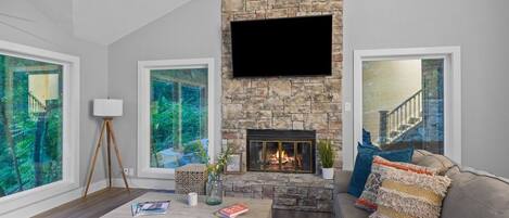 Una sala de estar con chimenea de piedra, ventanas amplias, televisor de pantalla plana y un rincón de estar acogedor.