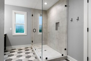 Un baño moderno con ducha envuelta en vidrio, ventana y suelo de baldosas.