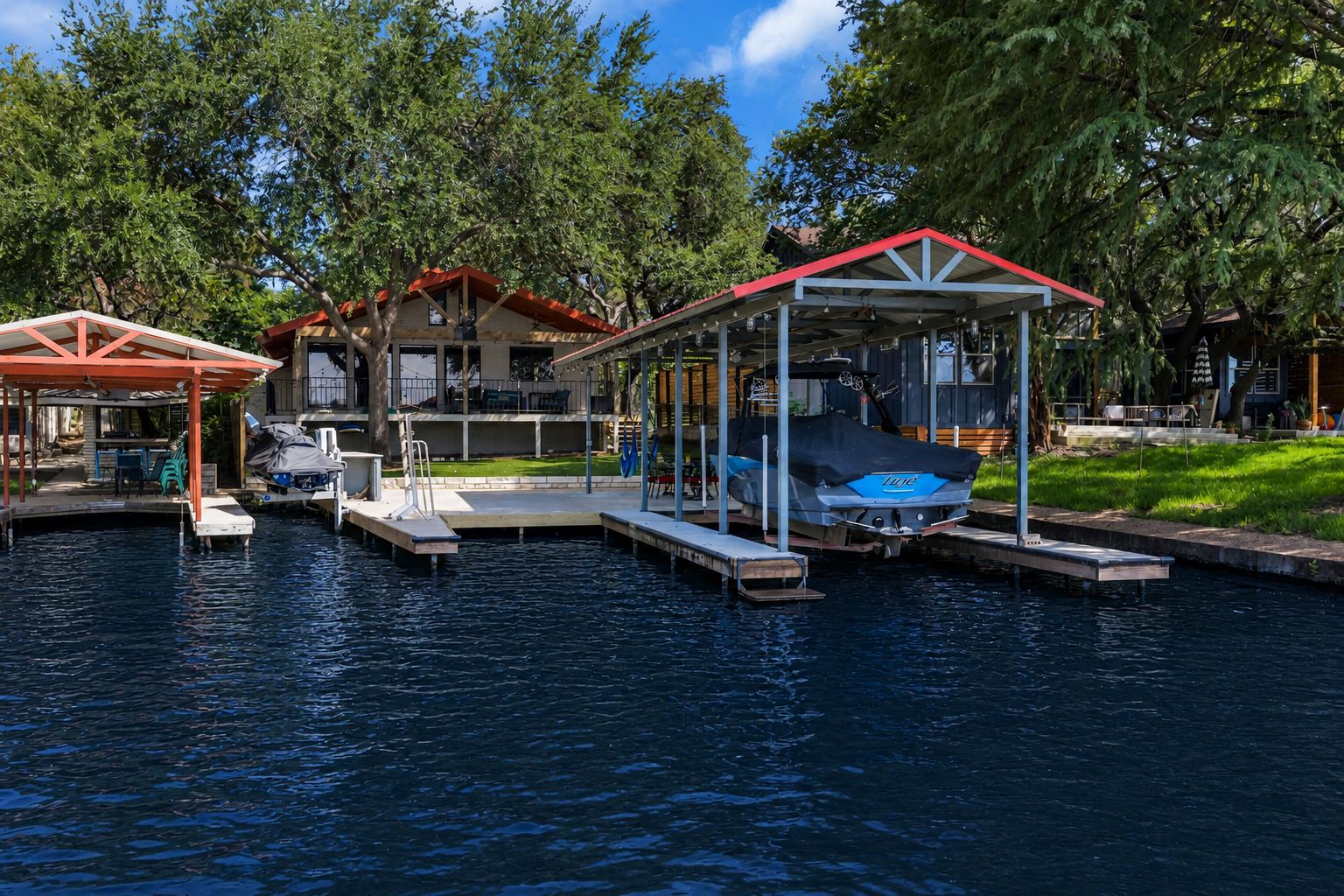 A waterfront property with a covered dock, a boat, and a building with a red roof.