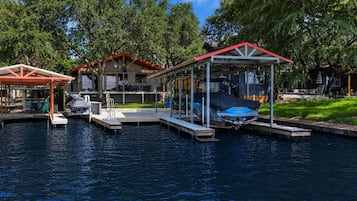 A waterfront property with a covered dock, a boat, and a building with a red roof.