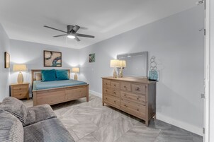 A bedroom with a bed, a dresser, a ceiling fan, and a nightstand.