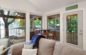 A cozy living room with a sofa, a coffee table, and a dining area with chairs and a table. There is a large window with a view of trees and a deck outside. - Lakefront Home - 3BR With Boat Dock (Marble Falls)