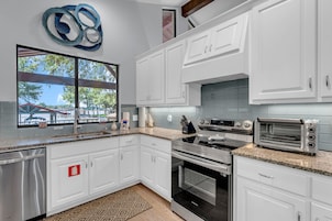A modern kitchen with white cabinets, stainless steel appliances, and a large window overlooking a marina.