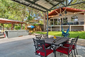 An outdoor patio with a table and chairs, a covered seating area, and a building with large windows in the background. - Lakefront Home - 3BR With Boat Dock (Marble Falls)