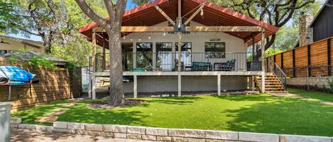 A two-story house with a covered patio, a stone staircase, and a fenced yard.
