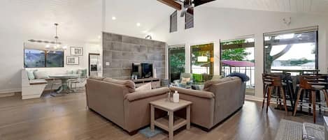 A modern living room with a sectional sofa, a TV, and a dining area with bar stools.
