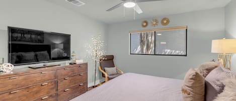 A bedroom with a bed, dresser, television, ceiling fan, window, and wall decorations.