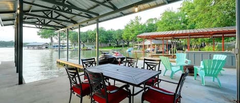 An outdoor covered seating area with tables and chairs, overlooking a body of water.
