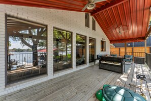 Una terraza techada con piso de madera, ventanas amplias y mobiliario exterior.