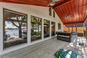 A covered deck with a wooden floor, large windows, and outdoor furniture.