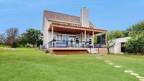Uma casa de dois andares com varanda coberta, chaminé e gramado bem cuidado.