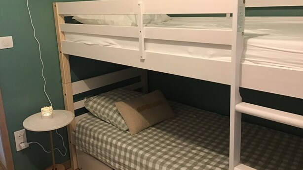 Un letto a castello con copripiumino a quadretti e cuscini, un piccolo tavolo rotondo con una lampada e una presa di corrente.