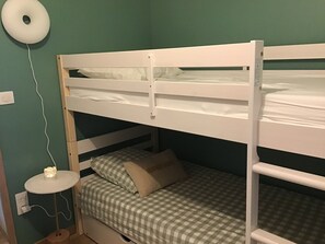 A bunk bed with a checkered bedspread and pillows, a small round table with a light, and a wall socket.