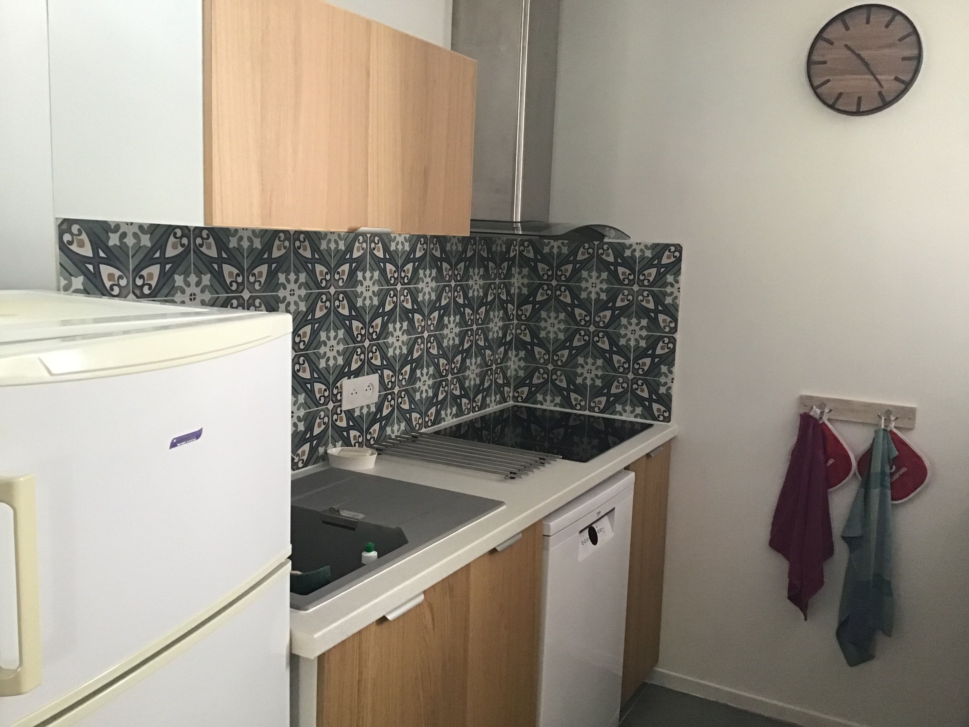 Une cuisine de taille réduite, équipée d’un réfrigérateur, d’un évier et d’une horloge fixée au mur.