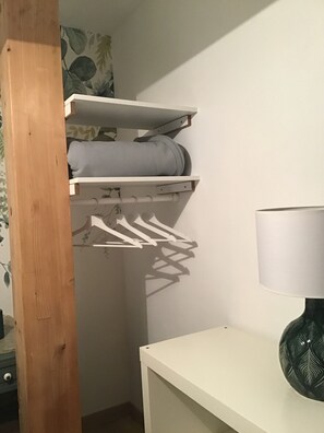 Un placard avec des étagères et une tringle pour suspendre les vêtements, une table blanche et une lampe.