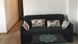 Un soggiorno con un divano nero, cuscini decorati, un tavolino in vetro e un tappeto geometrico.