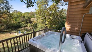 A hot tub on a wooden deck with a view of a forested area.