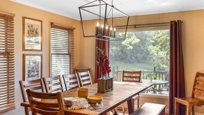 A dining room with a wooden table, chairs, a bench, a hanging light fixture, and a view of the outdoors.