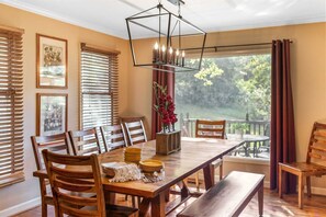 Un comedor con una mesa de madera, sillas, un banco, una lámpara colgante y vistas al exterior.