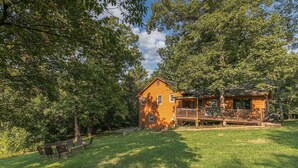 A wooden cabin with a porch, surrounded by trees and grass.