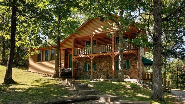 A wooden cabin with a stone foundation, a porch, and a staircase leading to the entrance.