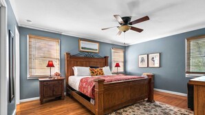 A bedroom with a wooden bed, two bedside tables with lamps, a ceiling fan, and a patterned rug.