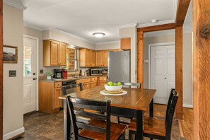 A kitchen with wooden cabinets, a stainless steel refrigerator, a dining table with chairs, and a bowl of green apples on the table. - Private Home on 3 Acres! 5 Bedrooms - Private Hot Tub - Close to Strip! | Silver Creek (Branson)