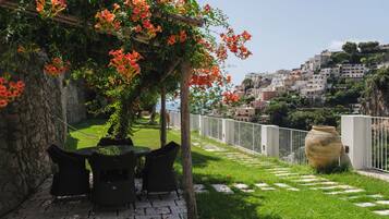 Un jardin agrémenté d’une pergola, d’un espace salon extérieur et offrant une vue sur une ville perchée sur une colline.