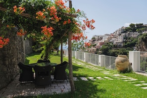 A garden with a pergola, outdoor seating, and a view of a hillside town. - Casacasa Positano (Campania)