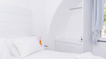 A modern, white-themed bedroom with a bed, a nightstand, a mirror, and a window with curtains.