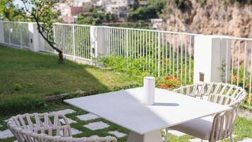 Un patio esterno con tavolo e sedie bianche, un recinto bianco e vista su un pendio con edifici.