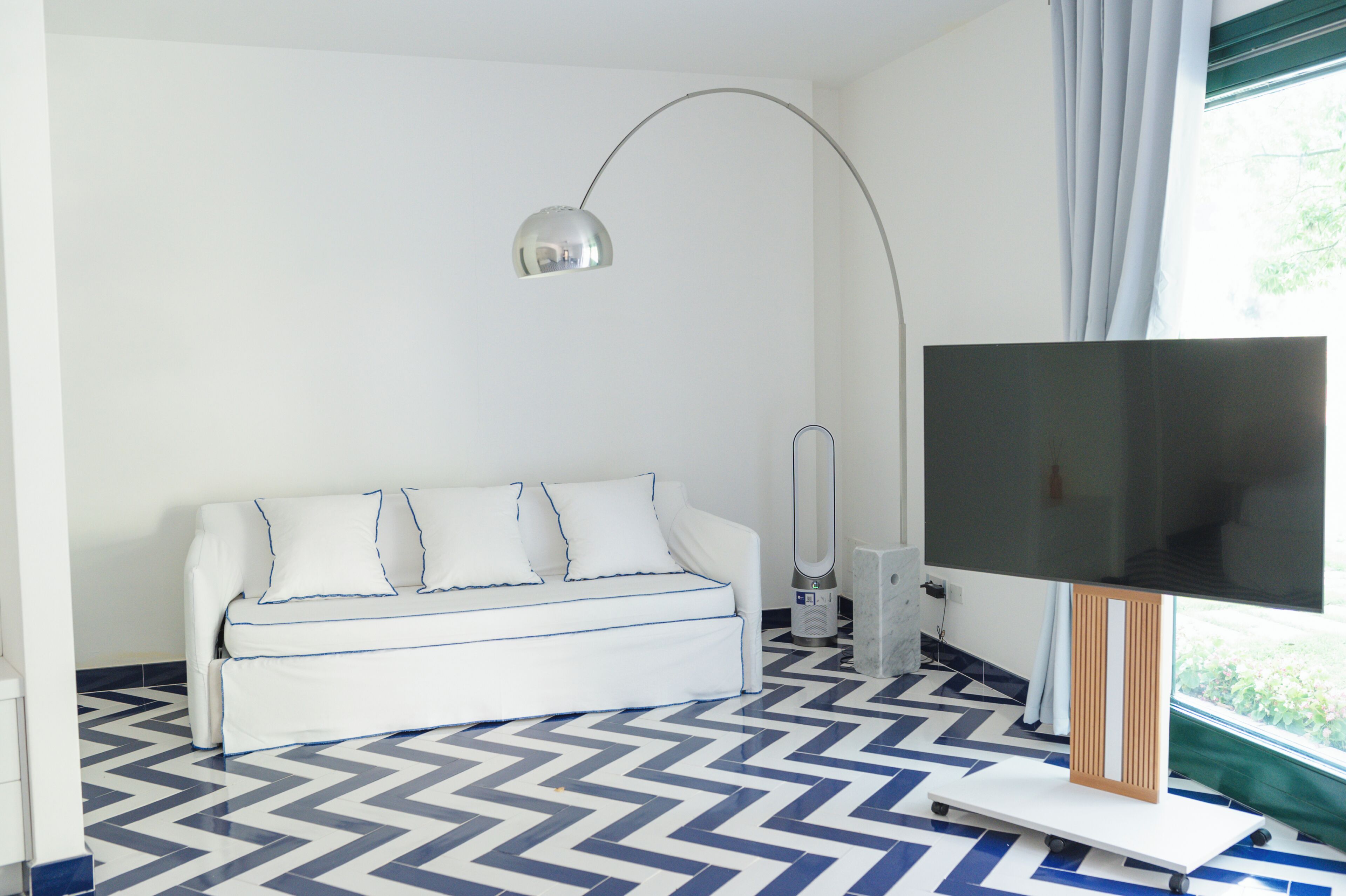 Un salon moderne avec un canapé, un lampadaire, un téléviseur à écran plat et un sol à motifs.
