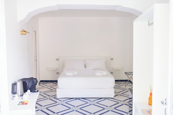 Una camera d'albergo con un letto, un comodino, una sedia, una lampada e un pavimento piastrellato.