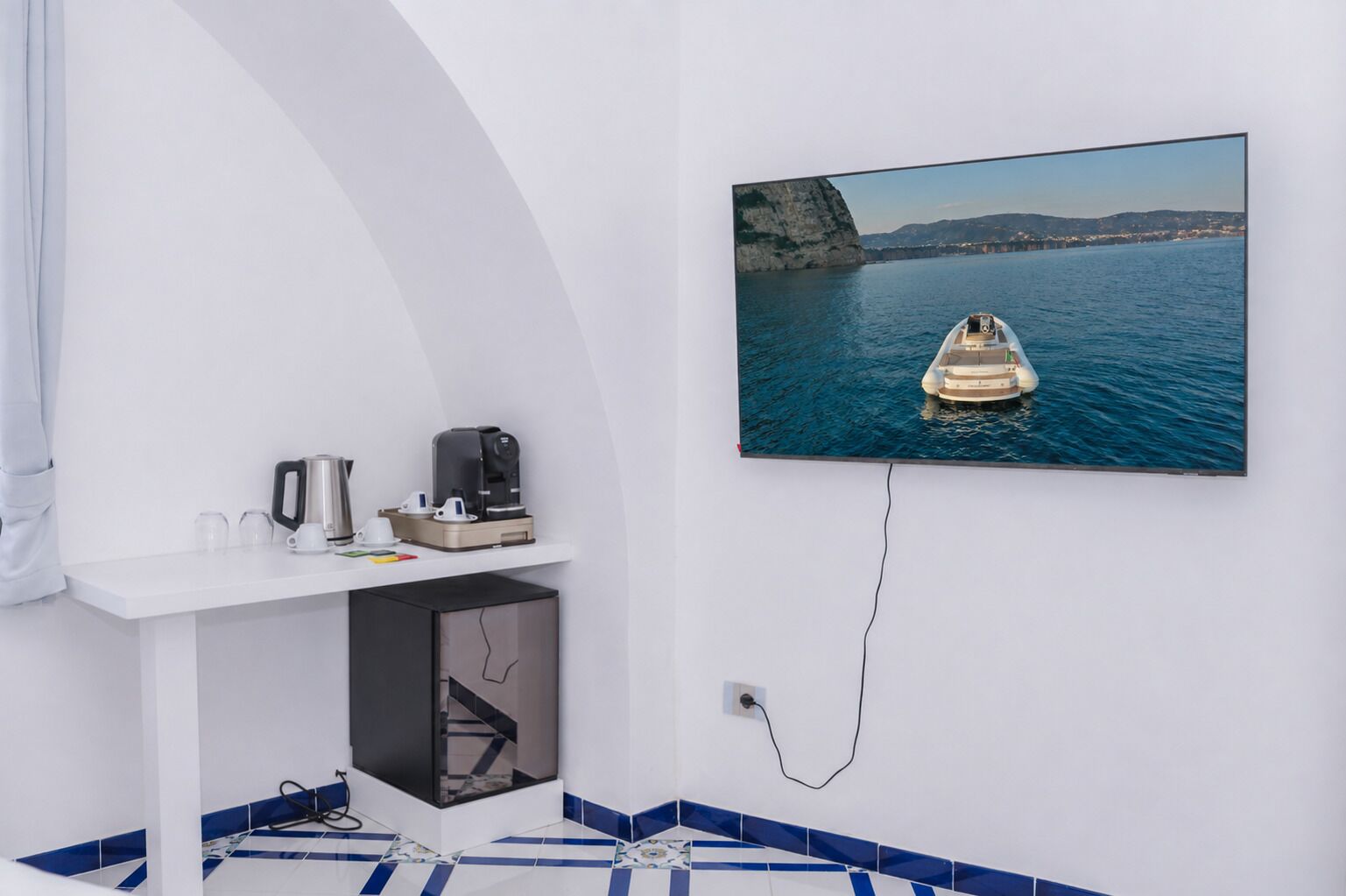 A modern room with a flat-screen TV mounted on the wall, a white console table with a coffee maker, and a small black cabinet.