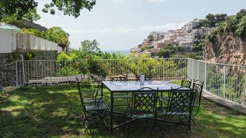 An outdoor patio with a table and chairs, surrounded by a white fence, overlooking a hillside with buildings.