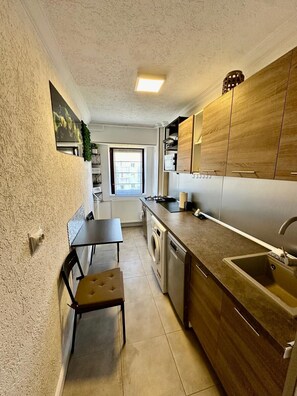A compact kitchen with a built-in washer, a small dining table, and a window providing natural light. - Studio 40 square metres, 2.2 km to the centre, 3.7 km to Palace of Parliament (București)