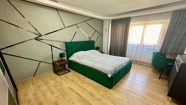 A room with a green upholstered bed, a wooden nightstand, a desk, and a chair.