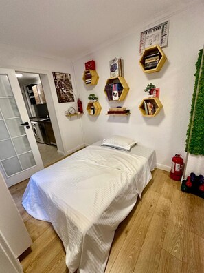A bedroom with a bed, a small shelf with books, a wall clock, and a fire extinguisher. - Studio 40 square metres, 2.2 km to the centre, 3.7 km to Palace of Parliament (București)