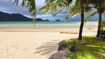 A beach with clear turquoise water, palm trees, and a large rock formation.