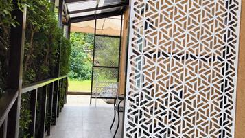 A corridor with a patterned screen, a tiled floor, and a view of greenery outside.