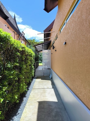 Un camino que lleva a un edificio con acceso cubierto, rodeado de vegetación y un cielo despejado.