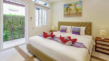 A hotel room with a large bed, a painting on the wall, and a balcony with a view of greenery.
