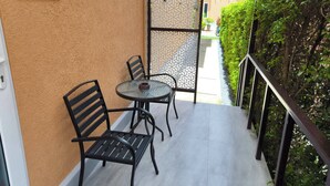 En balkon med to stole og et bord, et skilt med teksten 'GOLF' og udsigt til en bygning med rødt tag.