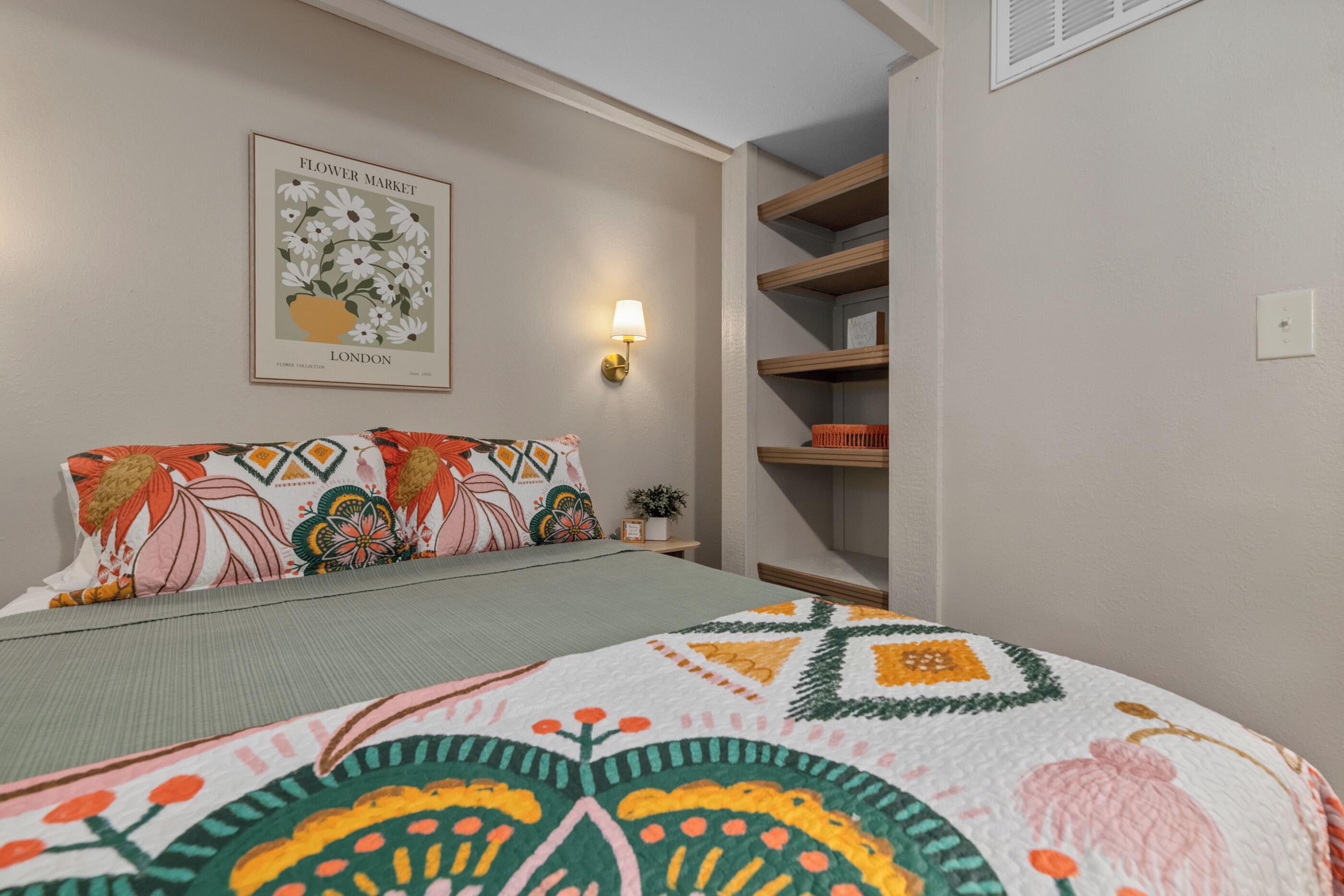 Ein Schlafzimmer mit einem Bett, Kissen, einer Wandleuchte und einem gerahmten Bild.