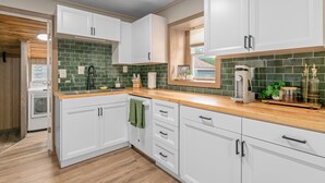 Una cocina moderna con armarios blancos, salpicadero de azulejos verdes y encimeras de madera.