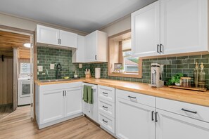 A modern kitchen with white cabinetry, a green tiled backsplash, and wooden countertops. - Easy Access to US-54 | Fenced Yard + W/D | Perfect for Travel Nurses! (Wichita)