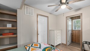 Un dormitorio con cama, ventilador de techo, cómoda y puerta que da a otra habitación.