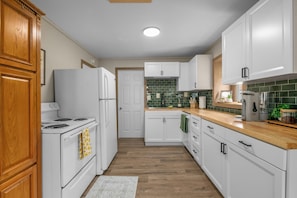 A kitchen with white cabinets, a wooden countertop, a stove, and a refrigerator. - Easy Access to US-54 | Fenced Yard + W/D | Perfect for Travel Nurses! (Wichita)
