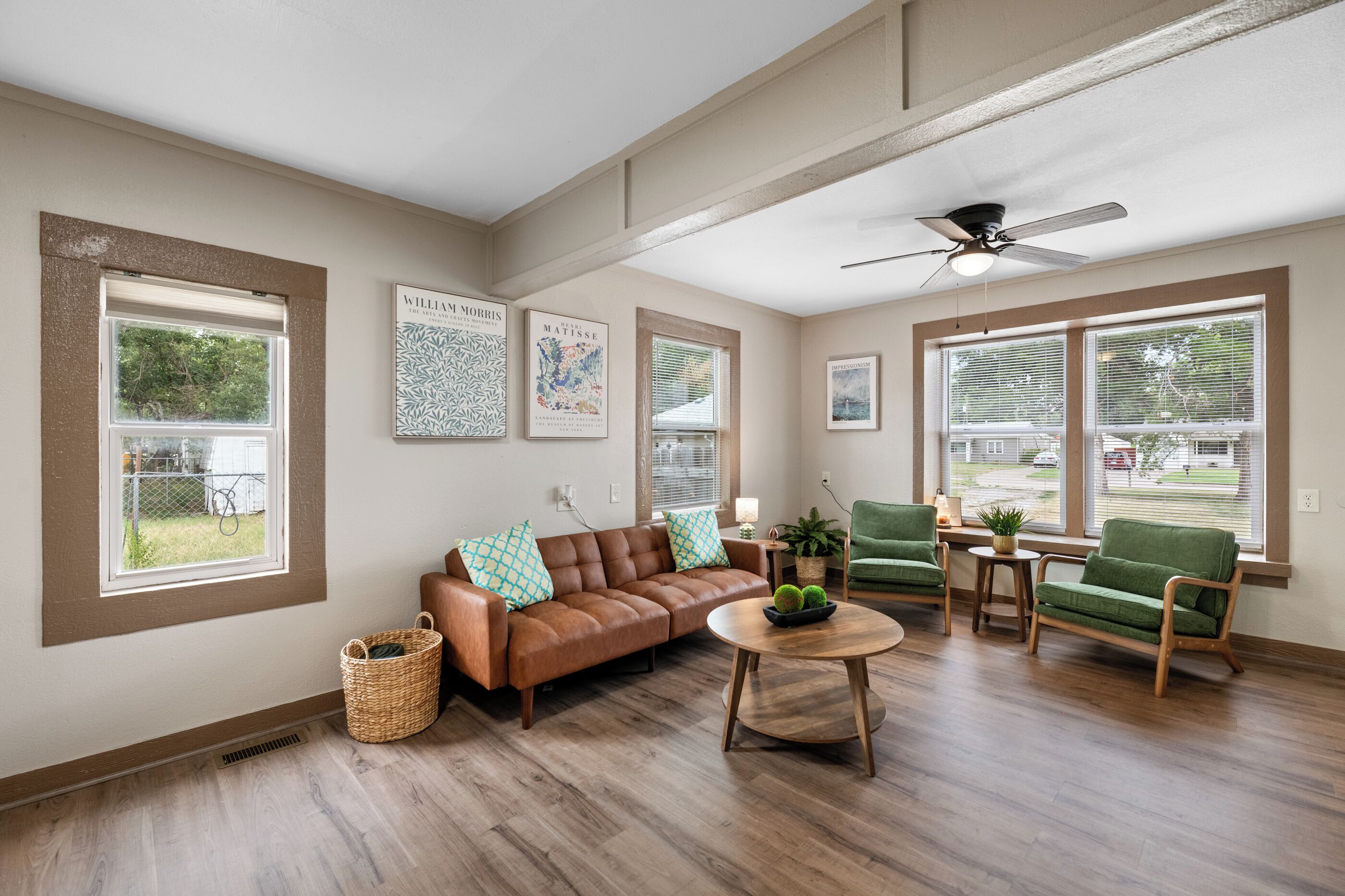 A spacious living room with a brown leather sofa, green armchairs, a round wooden coffee table, and artwork on the walls.